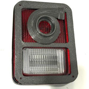 Könnte beinhalten: Ein rechteckiger Fahrzeug-Rücklicht-Baugruppe mit schwarzem Rahmen. Die Baugruppe verfügt über einen roten Innenbereich, eine klare Linse und eine kreisförmige schwarze Komponente. Das Rücklicht ist für den Automobilgebrauch konzipiert.