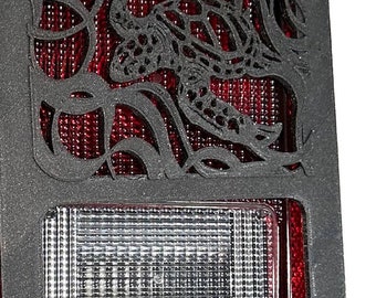 May include: Black Jeep Wrangler tail light cover with a cutout design of a turtle in a vine. The cover is made of a durable material and is designed to protect the tail light from damage.