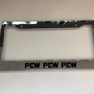 May include: Chrome license plate frame with the text "PEW PEW PEW" in black lettering.