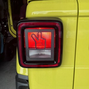 May include: A yellow Jeep with a black and red taillight. The taillight has a peace sign cutout in the center.