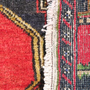 May include: Close-up of a red, black, and white patterned rug with a fringe edge. The rug has a geometric design with a central red square.