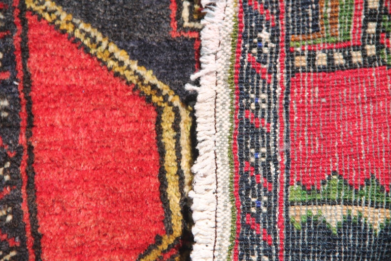 May include: Close-up of a red, black, and white patterned rug with a fringe edge. The rug has a geometric design with a central red square.