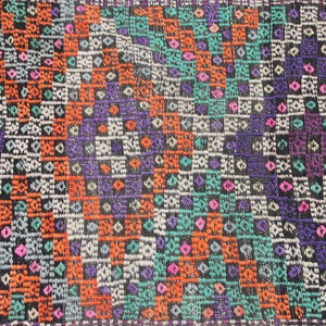 May include: A close-up of a colourful woven rug with a geometric pattern. The rug features shades of orange, blue, green, purple, and white.