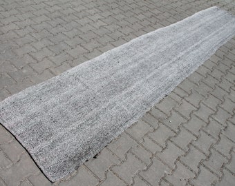May include: A long, grey and white woven rug laid out on a grey concrete surface.