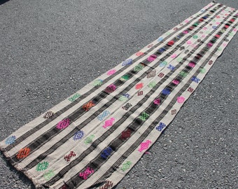 Könnte beinhalten: Ein langer, weißer Läufer mit schwarzen Streifen und bunten geometrischen Mustern. Der Teppich ist traditionell gewebt und hat einen rustikalen, Vintage-Look.