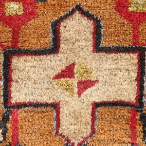 May include: Close-up of a brown, beige, red, and black patterned rug with a central cross-shaped design.