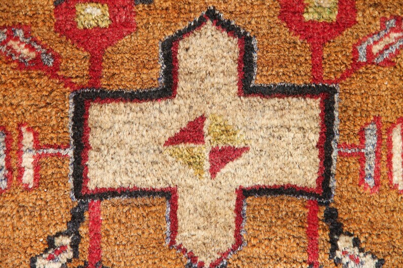 May include: Close-up of a brown, beige, red, and black patterned rug with a central cross-shaped design.