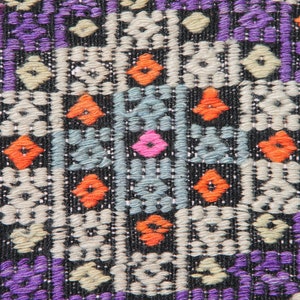 May include: Close-up of a colourful woven fabric with a geometric pattern. The fabric is primarily black with purple, orange, white, and blue accents.