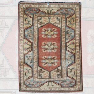 Puede incluir: Alfombra rectangular con un panel central rojo con motivos florales. La alfombra tiene un fondo beige con un borde azul y diseños geométricos intrincados. La alfombra probablemente está hecha de tela tejida.