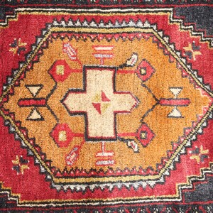 May include: A red, black, and gold patterned rug with a central design featuring a cross shape. The rug has a traditional, intricate design.