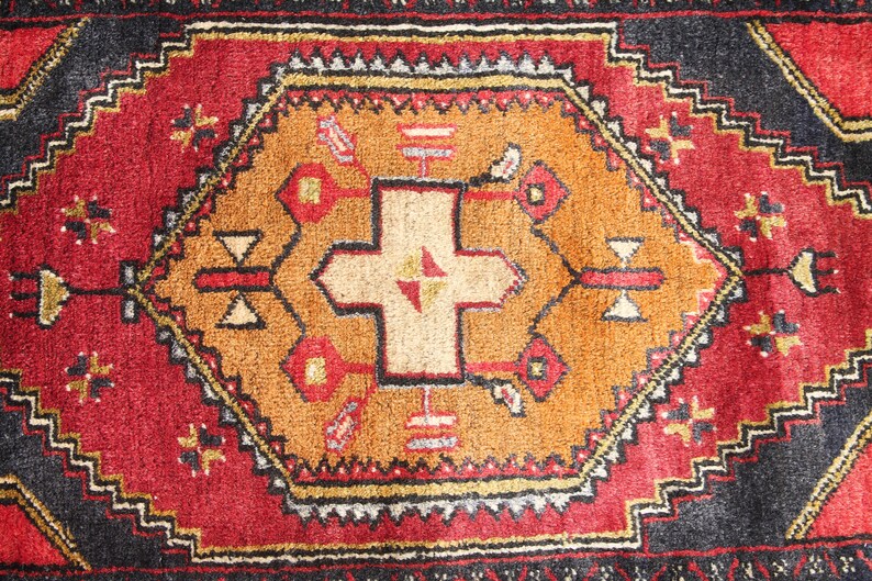 May include: A red, black, and gold patterned rug with a central design featuring a cross shape. The rug has a traditional, intricate design.