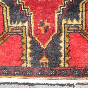 May include: Close-up of a red rug with a black and gold geometric pattern. The rug has a fringe border.