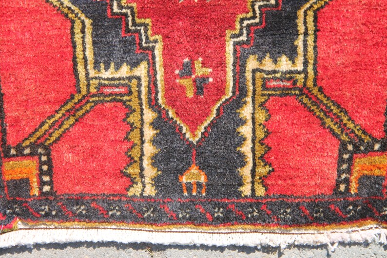 May include: Close-up of a red rug with a black and gold geometric pattern. The rug has a fringe border.