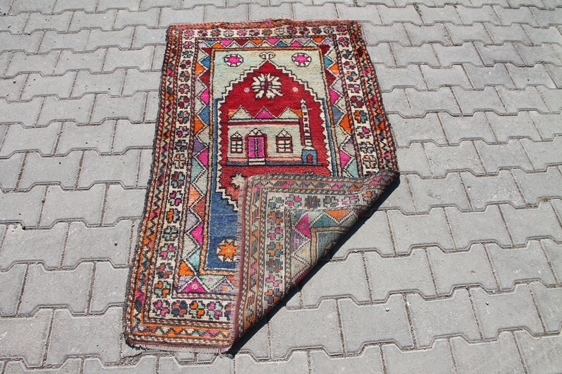 Pu&ograve; includere: Un tappeto da preghiera turco vintage colorato con un motivo di moschea al centro. Il tappeto &egrave; piegato a met&agrave; e ha un aspetto usurato e rovinato.