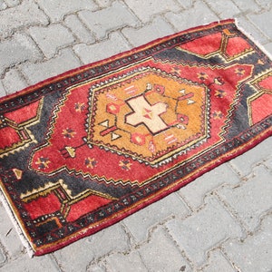 May include: A red, orange, and black patterned rug with a geometric design. The rug is fringed on all sides.