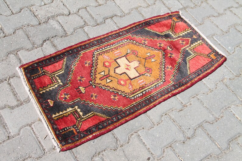 May include: A red, orange, and black patterned rug with a geometric design. The rug is fringed on all sides.
