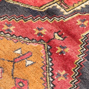 May include: Close-up of a colorful rug with intricate geometric patterns in shades of red, orange, black, and white.