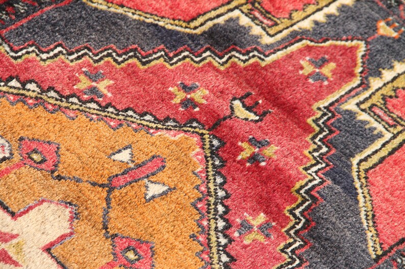 May include: Close-up of a colorful rug with intricate geometric patterns in shades of red, orange, black, and white.