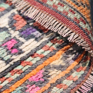 Pu&ograve; includere: Primo piano di un tappeto tessuto colorato con un bordo a frangia. Il tappeto ha una variet&agrave; di colori, tra cui arancione, rosa, blu e verde.