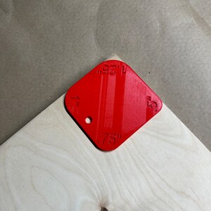 May include: Red plastic ruler with markings for 1/4 inch, 1/2 inch, 3/4 inch, and 1 inch. The ruler is on a light wood surface.
