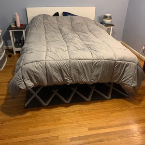 May include: A gray comforter on a white bed frame with a gray and white patterned rug on a hardwood floor. There are two nightstands with lamps on either side of the bed.