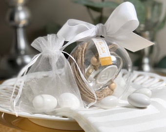May include: A clear glass sphere ornament with a white ribbon and a tag that reads "Mr. & Mrs. Smith - Tied the Knot - 5-8-2014". The ornament is filled with twine and small wooden beads. The ornament is sitting on a white plate with white candy.