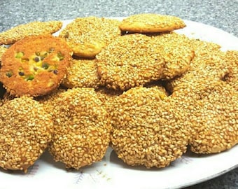May include: A plate of golden brown sesame seed cookies. Some of the cookies have a light green color from pistachios.