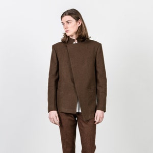 Könnte beinhalten: Ein brauner Blazer mit einem Stehkragen und einem diagonalen Verschluss. Der Blazer hat einen strukturierten Stoff und eine einzelne Tasche auf der linken Seite.