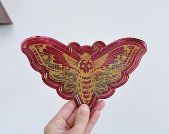 May include: A red resin tray with a gold moth design. The moth has a skull and crossbones on its head.