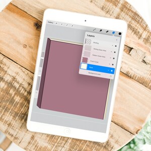 Może przedstawiać: Biały tablet wyświetla cyfrową ilustrację książki z malinową okładką i złotymi obramowaniami. Ekran pokazuje panel warstw z opcjami dla oprawy, pisania i okładki. Tablet spoczywa na drewnianej powierzchni.
