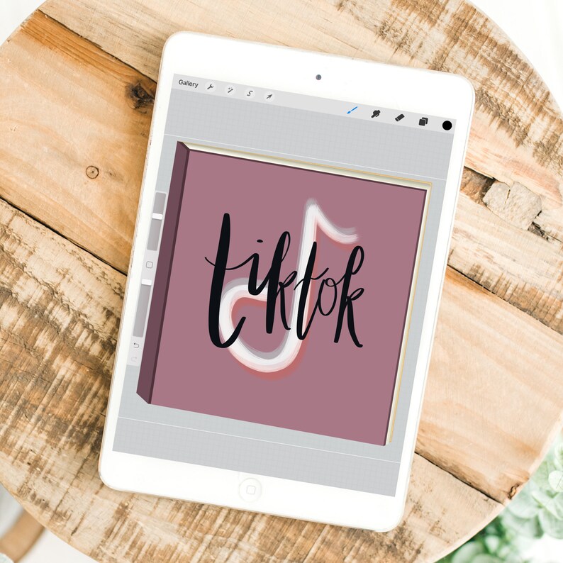 Może przedstawiać: Biały tablet wyświetlający cyfrową ilustrację logo TikTok. Logo zawiera słowo "tiktok" w stylu odręcznym, ze stylizowaną nutą muzyczną. Tło jest w stonowanym kolorze malwy.