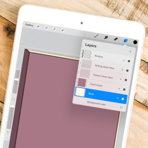 Może przedstawiać: Cyfrowa ilustracja projektu książki na tablecie. Ekran wyświetla układ książki z warstwami do oprawy, pisania i okładki. Schemat kolor&oacute;w to gł&oacute;wnie stonowane r&oacute;że i kremy, z drewnianym tłem.