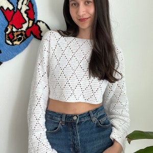 May include: White crochet top with a loose, cropped fit and bell sleeves. The top has a delicate, open-stitch pattern.