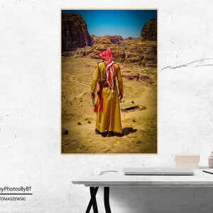Puede incluir: Un hombre con una t&uacute;nica amarilla y un turbante rojo se encuentra en un paisaje des&eacute;rtico. El paisaje es rocoso y &aacute;rido, con algunos &aacute;rboles y arbustos peque&ntilde;os. El hombre mira hacia el horizonte.