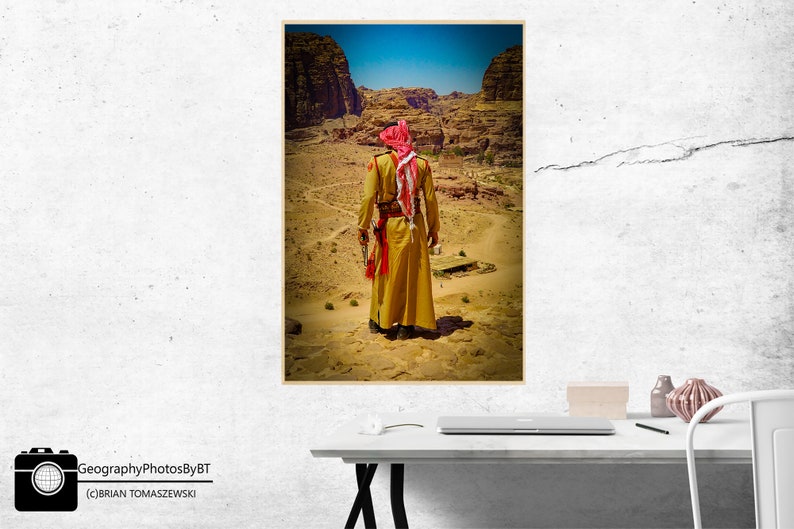 Puede incluir: Un hombre con una t&uacute;nica amarilla y un turbante rojo se encuentra en un paisaje des&eacute;rtico. El paisaje es rocoso y &aacute;rido, con algunos &aacute;rboles y arbustos peque&ntilde;os. El hombre mira hacia el horizonte.