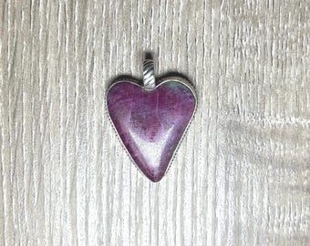 May include: A heart-shaped pendant with a silver-colored border and bail. The pendant's center features a deep magenta stone with a textured surface. The bail has a twisted design.