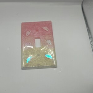 Puede incluir: Una tapa de interruptor de luz con un dise&ntilde;o degradado rosa y blanco y detalles de nubes iridiscentes.