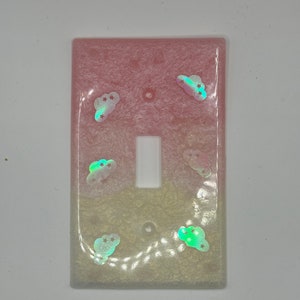 Puede incluir: Una tapa de interruptor de luz en degradado rosa y blanco con nubes y estrellas iridiscentes.