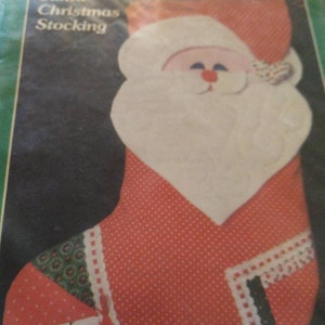 May include: A red and white Santa Claus Christmas stocking with a white beard and a red nose. The stocking has a green and white patterned trim.