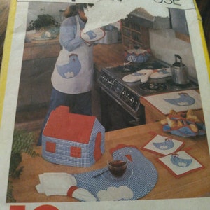 May include: A Simplicity House sewing pattern for 10 kitchen items, including a red and blue gingham house-shaped pot holder, a chicken-shaped trivet, and a set of oven mitts. The pattern also includes instructions for making a set of matching placemats and napkins.