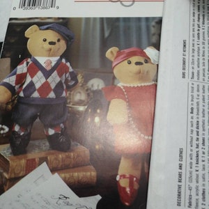 May include: A Simplicity sewing pattern for making decorative bears and clothes. The pattern number is 0660. The pattern shows two bears, one wearing a red dress and the other wearing a blue and red sweater. The bears are sitting on a stack of books.