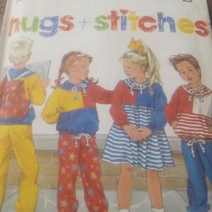 May include: A vintage Simplicity sewing pattern titled "hugs + stitches." The pattern features illustrations of children in colorful outfits, including a blue and white striped dress, star-patterned pants, and a red and white striped top.