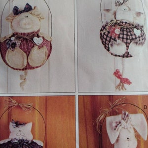 May include: Four handmade fabric ornaments, each featuring a different animal. The ornaments are a pig, a cat, a cat, and a bunny. Each ornament is wearing a dress and has a bow on its head. The ornaments are hanging from a wire loop.