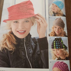 May include: A Simplicity sewing pattern envelope 1959 for hats in sizes S, M, L. The front displays a red ribbed hat, a blue hat with a floral detail, a brown folded hat, a black hat with colorful polka dots, and a pink ribbed hat with text.