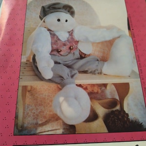 May include: A 24-inch muslin rabbit doll named Andrew, wearing a gray hat, a vest with a floral pattern, and gray pants. The doll is sitting on a wooden chair with a wooden shoe and a pine cone beside it.