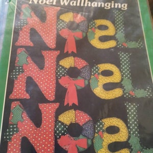 May include: A craft pattern for a wall hanging that says "Noel" in large letters. The letters are made of fabric and decorated with wreaths and bows. The pattern includes full-size patterns and instructions.
