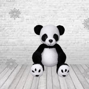 May include: A crocheted panda bear plush toy with black and white fur. The panda is sitting with its paws in front of it.