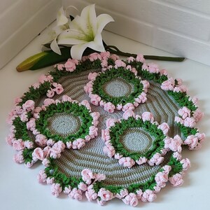 K&ouml;nnte beinhalten: Set aus vier geh&auml;kelten Untersetzern mit einem gr&uuml;n-grauen Streifenmuster und rosa Blumenakzenten.