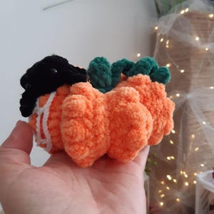 May include: A crocheted pumpkin with a black hat and green stem. The pumpkin is made of orange yarn and has a fluffy texture.