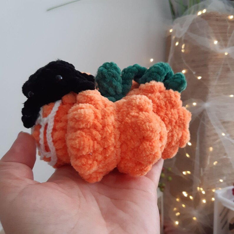 May include: A crocheted pumpkin with a black hat and green stem. The pumpkin is made of orange yarn and has a fluffy texture.